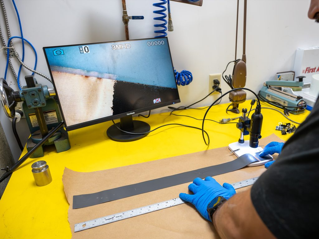 A CEI technician inspects a coated electrode strip under a digital microscope